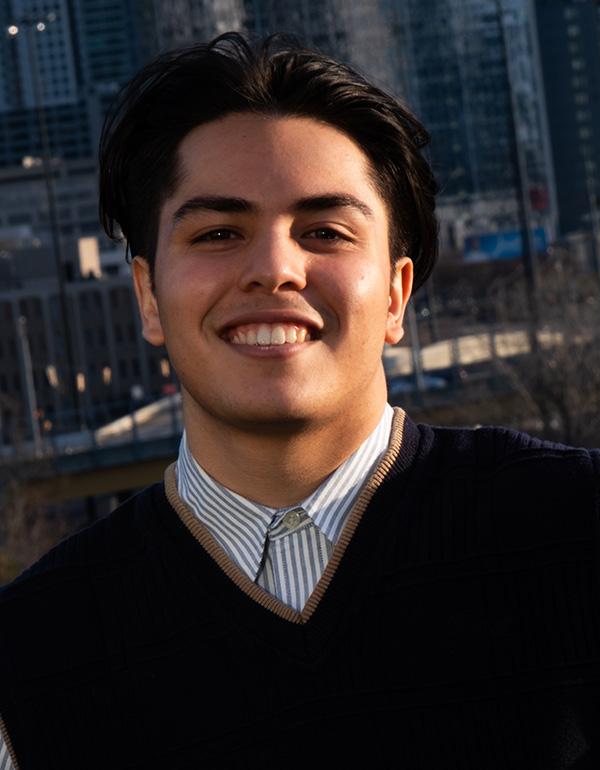 Man in a black vest with short black hair smiling.